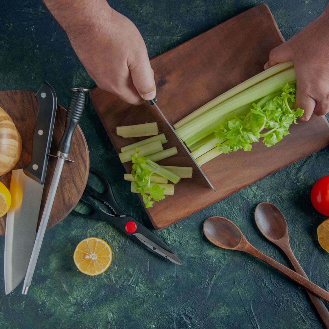 Person cutting celery on a wooden cutting board with kitchen utensils on a green surface