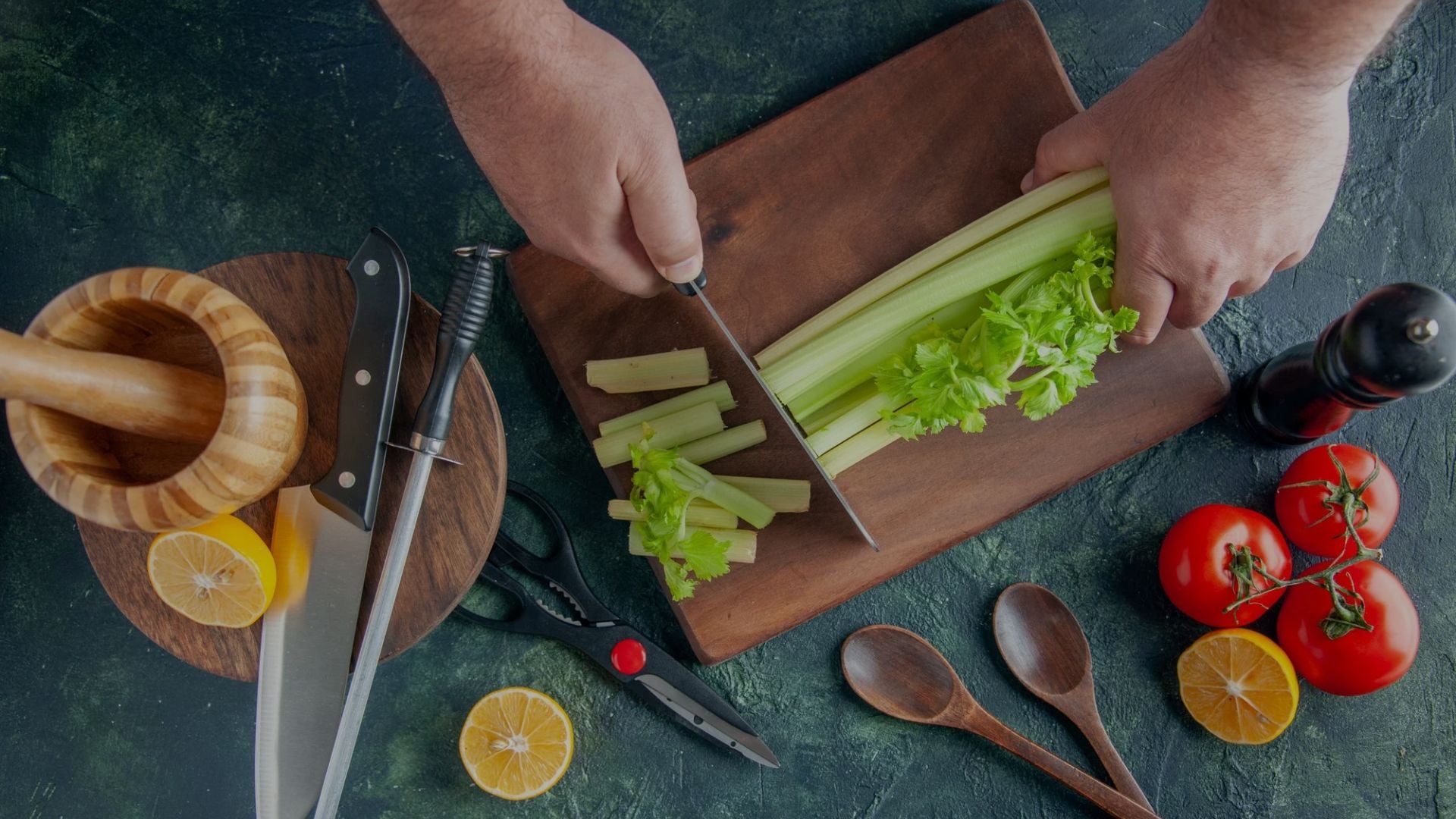Person cutting celery on a wooden cutting board with kitchen utensils on a green surface