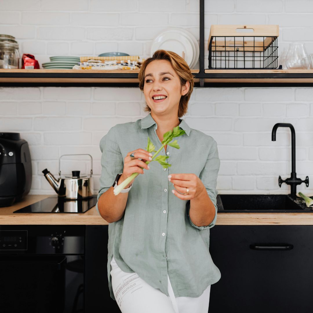 Woman holding a bunch of green vegetables in a kitchen.